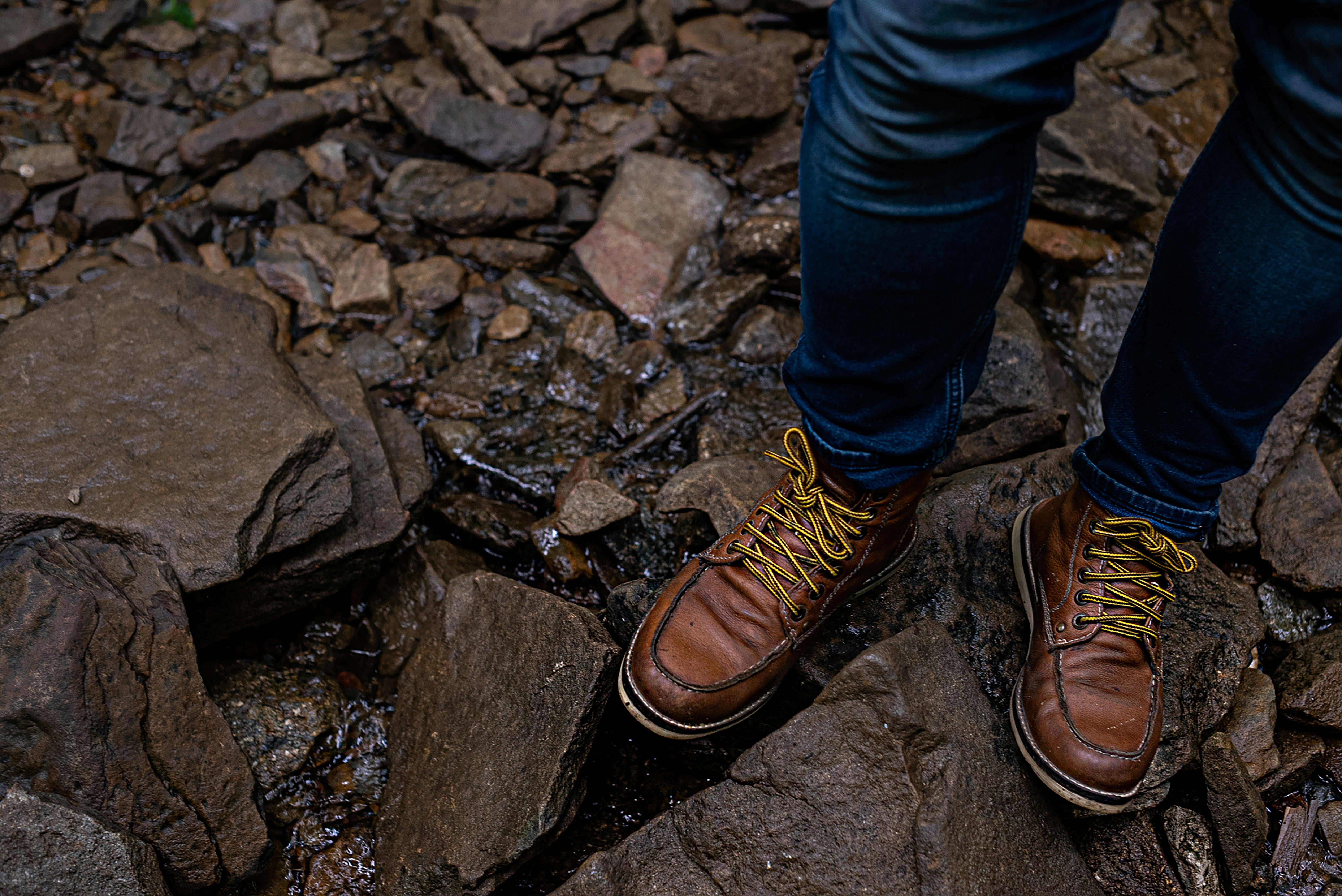 person in blue denim jeans and brown leather shoes standing on rocky ground